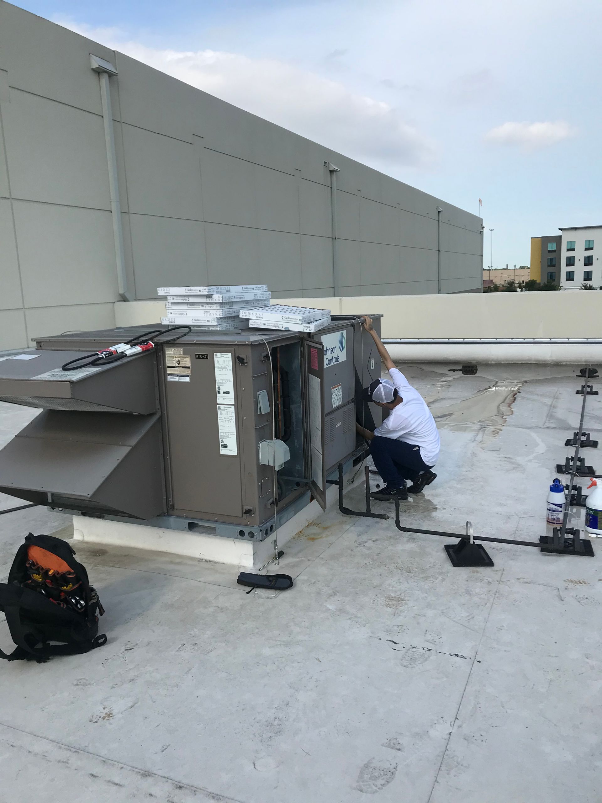 A man is working on an air conditioner on the roof of a building.