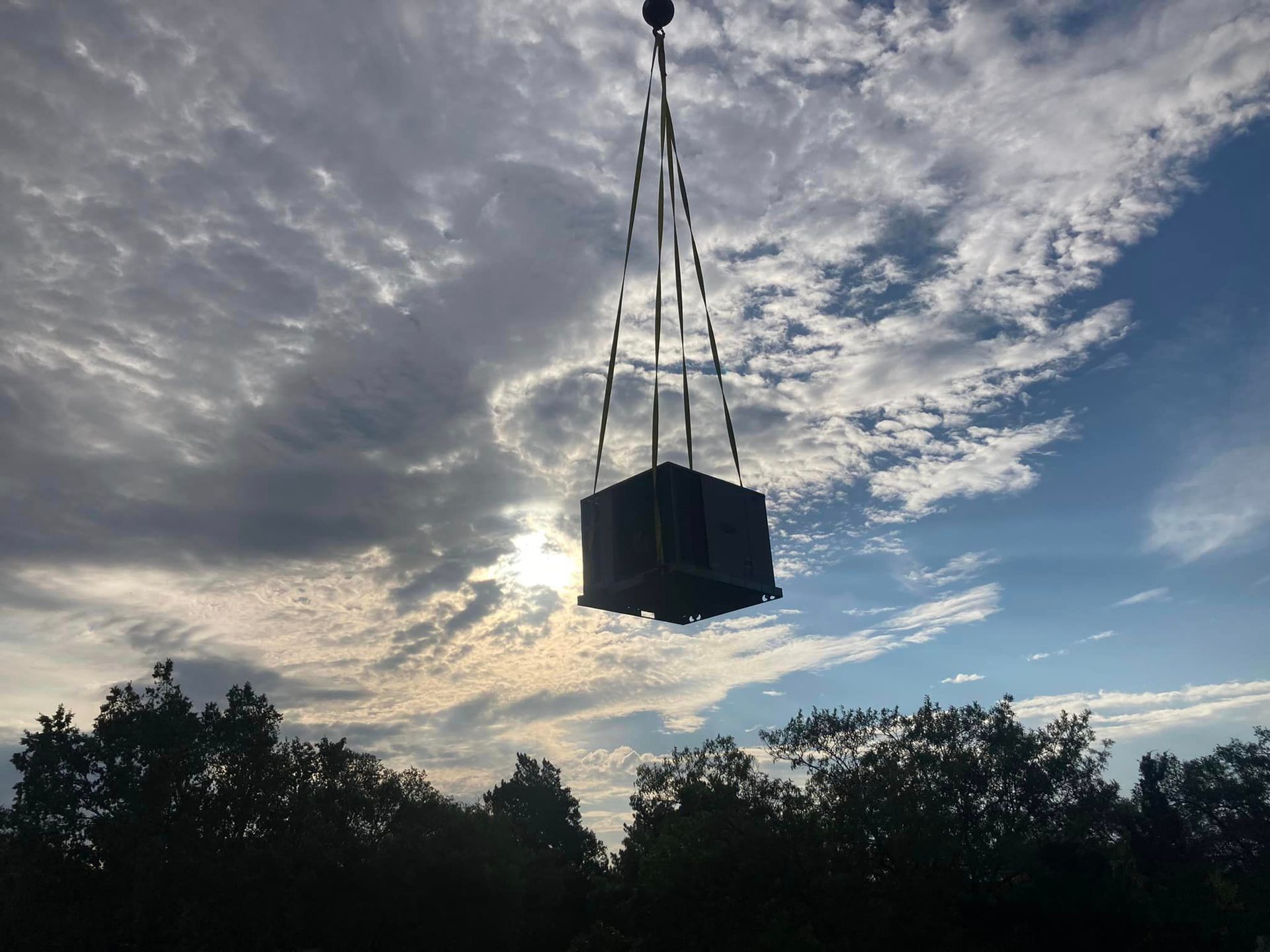 A large cube is hanging from a crane in the sky.