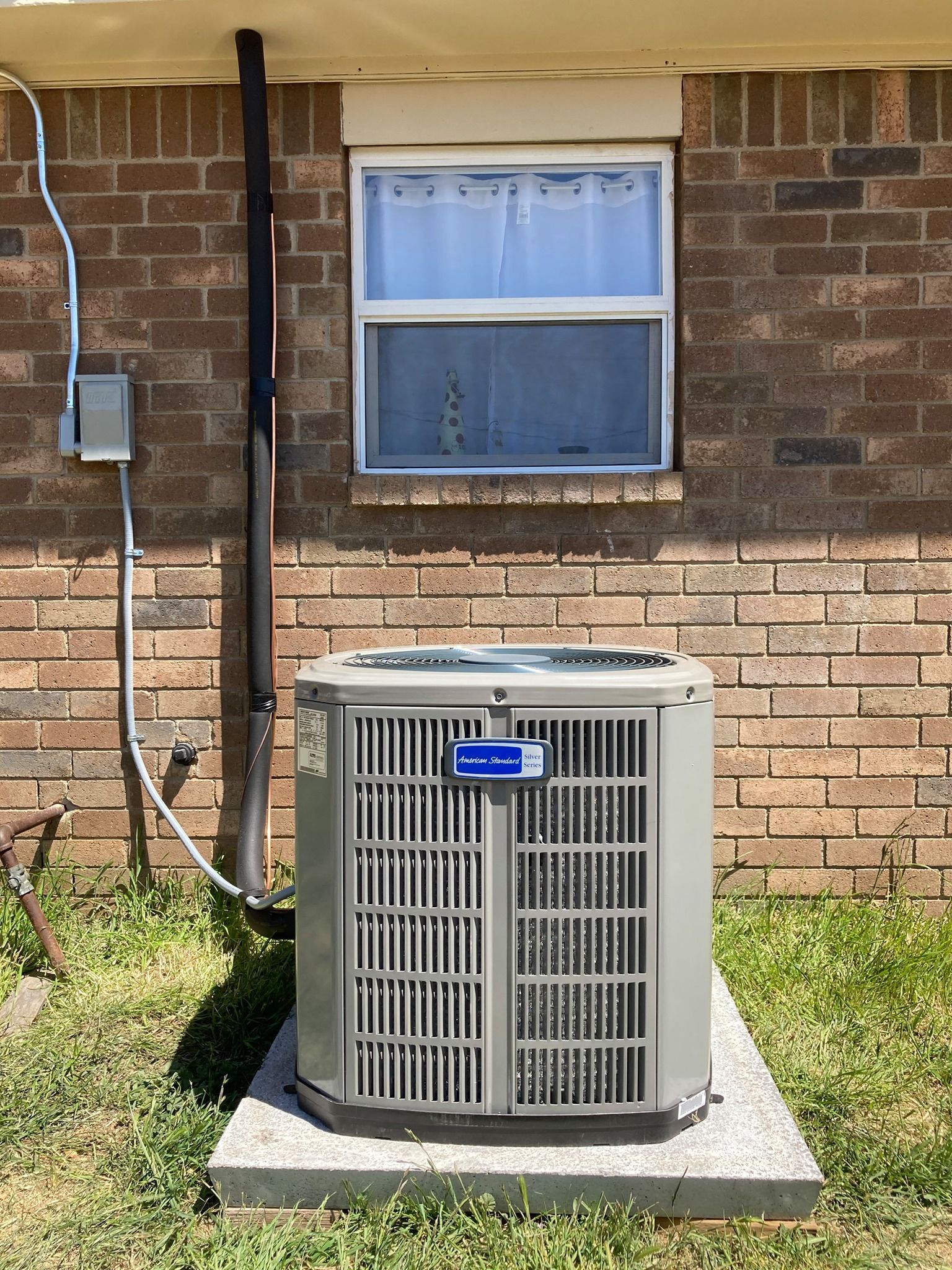 An air conditioner is sitting outside of a brick building next to a window.
