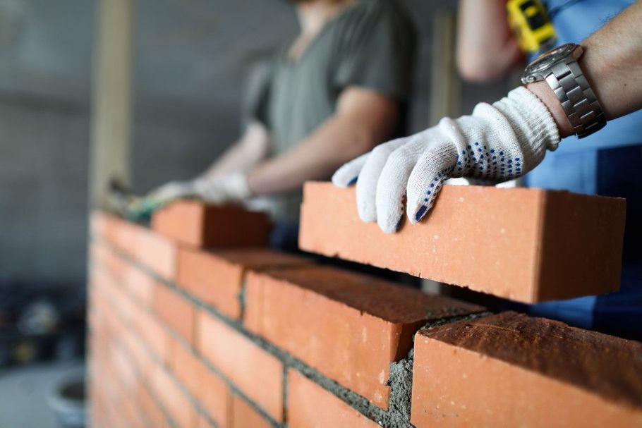 Gloved hands laying red bricks to build a wall outdoors