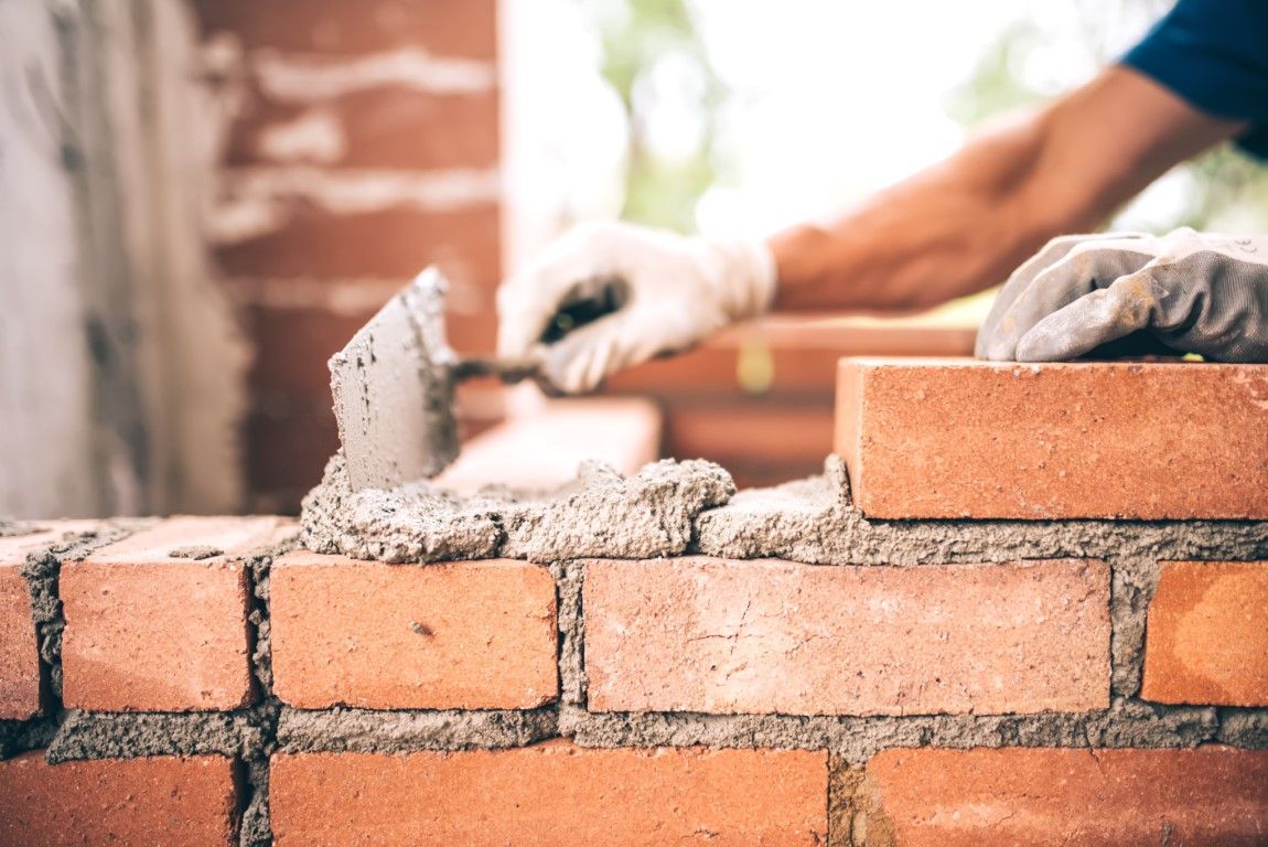 Hands laying bricks with mortar on a wall under construction