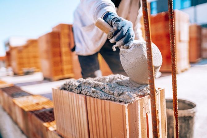 Construction worker pouring concrete into a brick wall mold outdoors