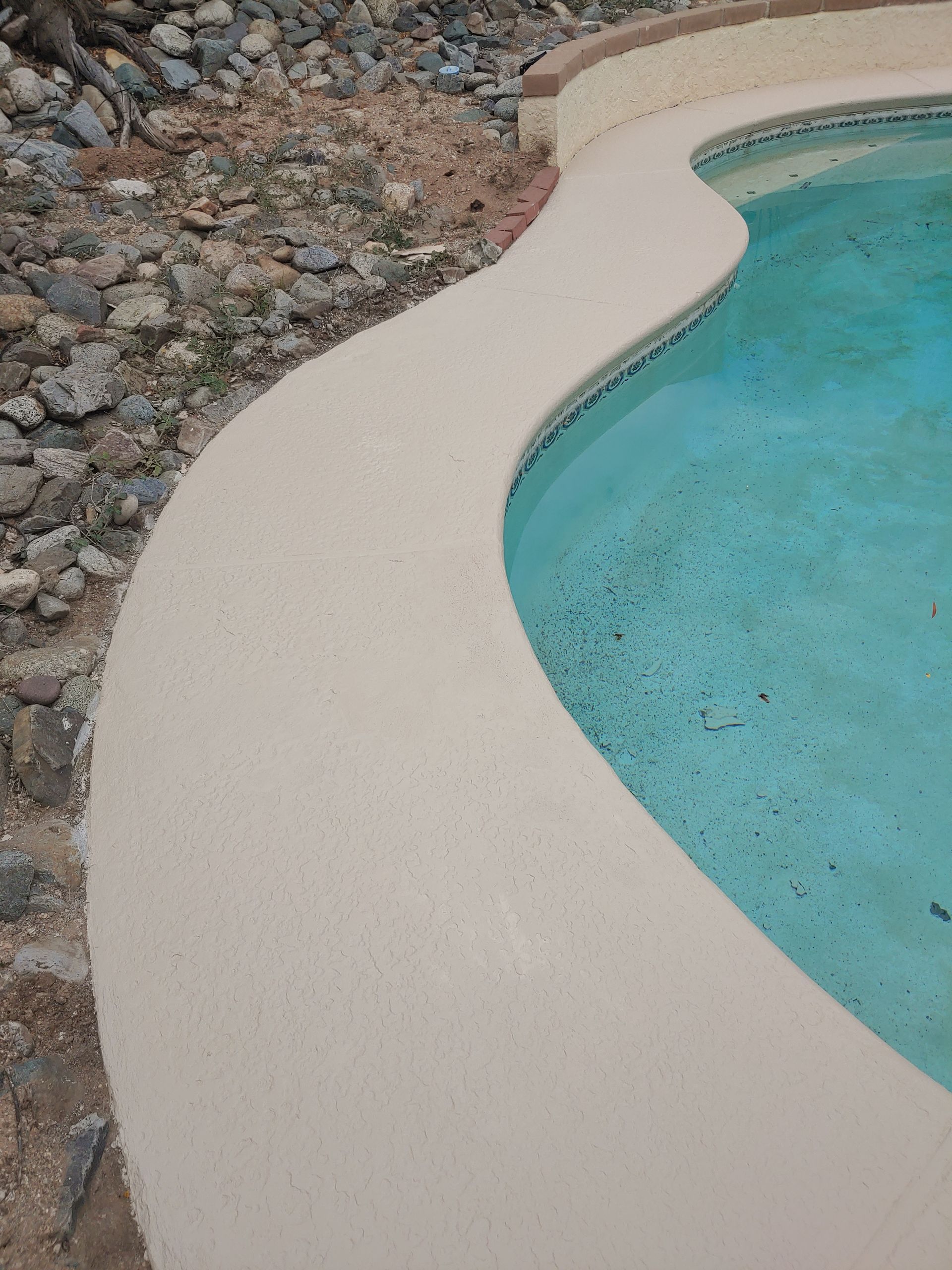 A swimming pool is surrounded by rocks and a concrete border