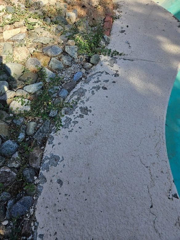 A concrete walkway next to a pool with rocks on the side of it.