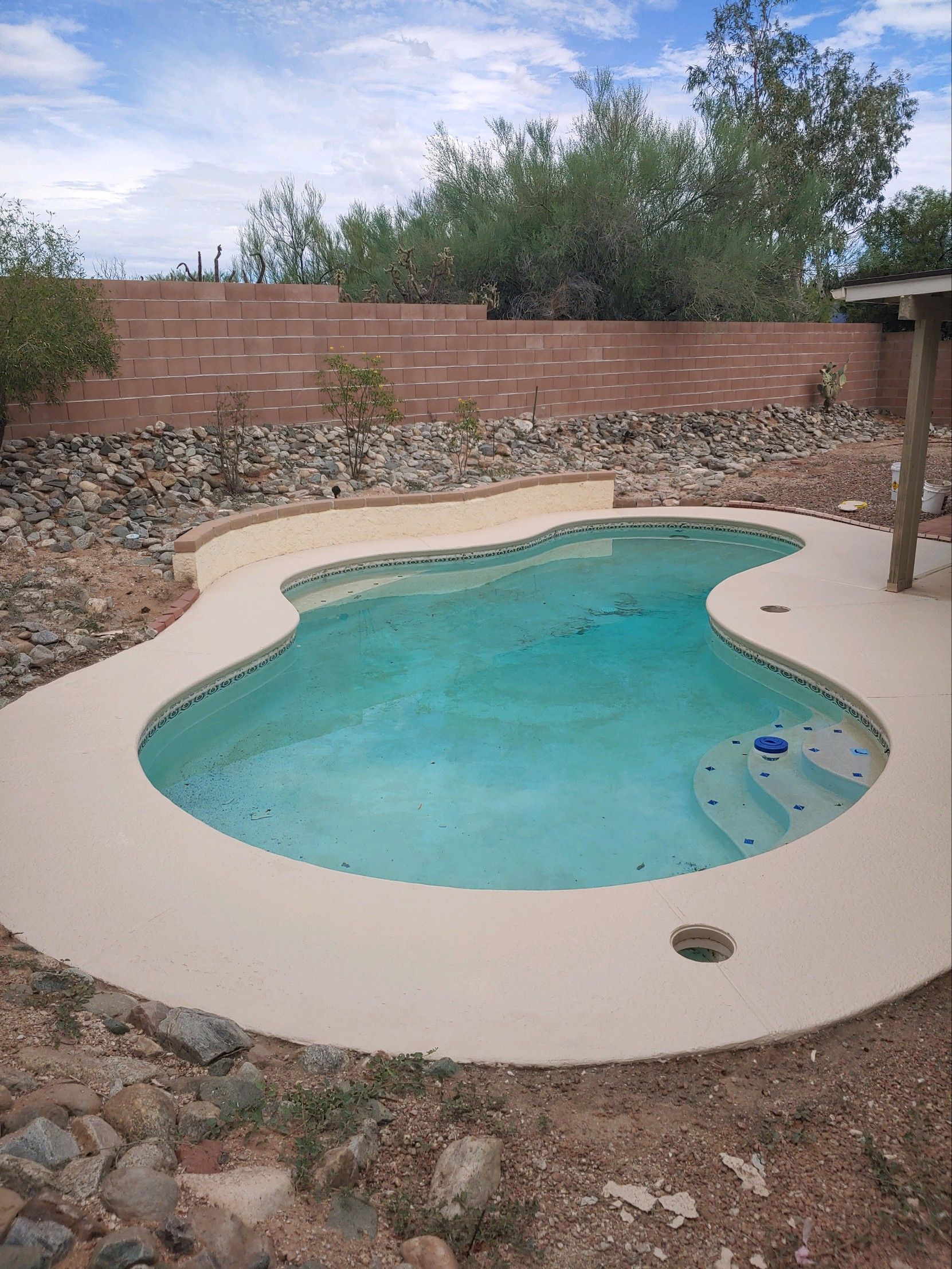 A large swimming pool surrounded by rocks and trees in a backyard.