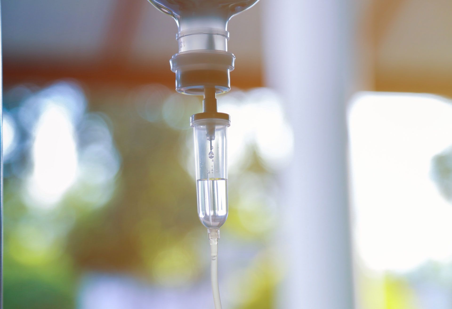 IV drip with clear fluid dripping, blurred green background.