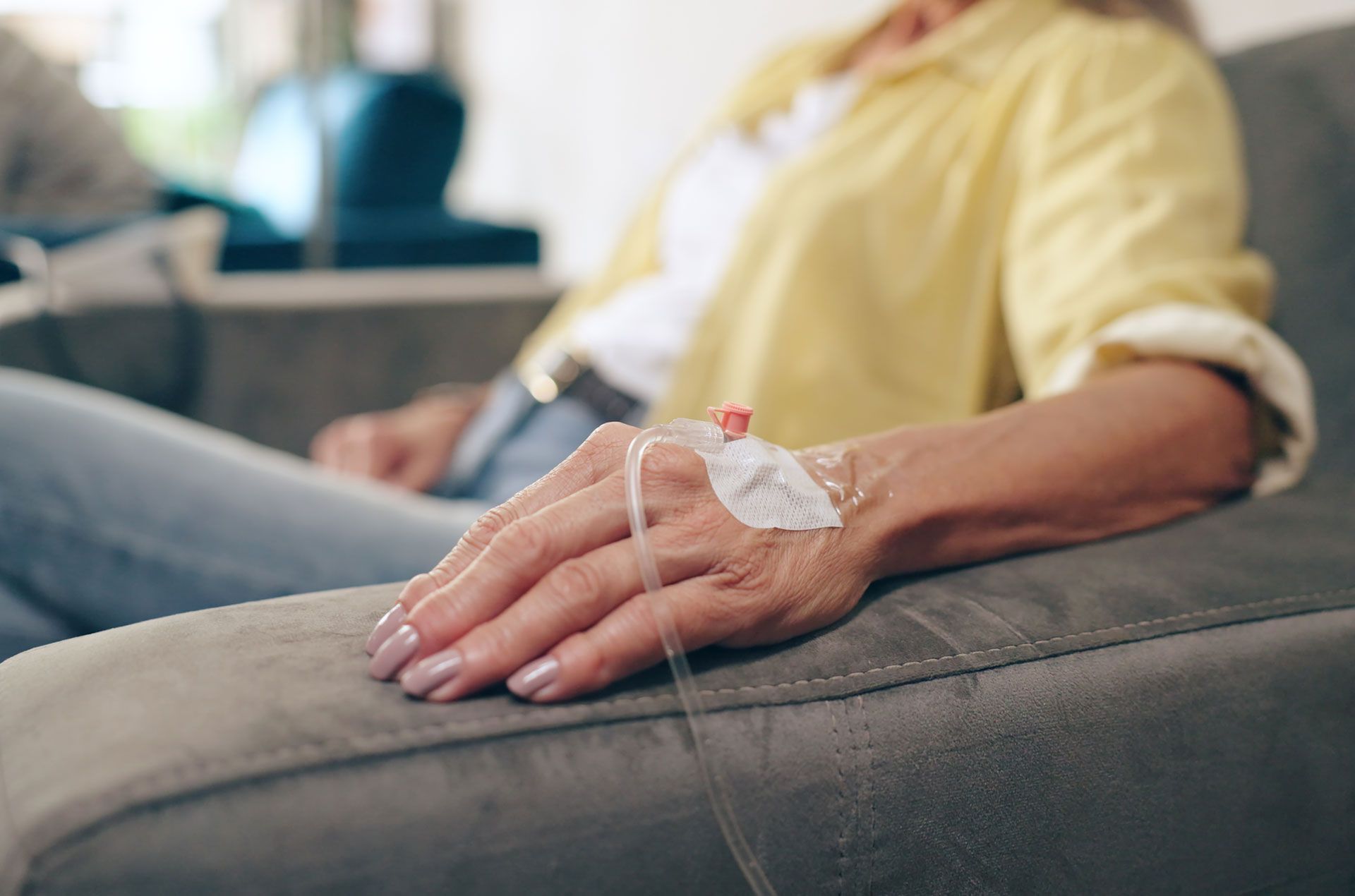 Person receiving intravenous fluids, hand resting on a gray couch, IV line visible.