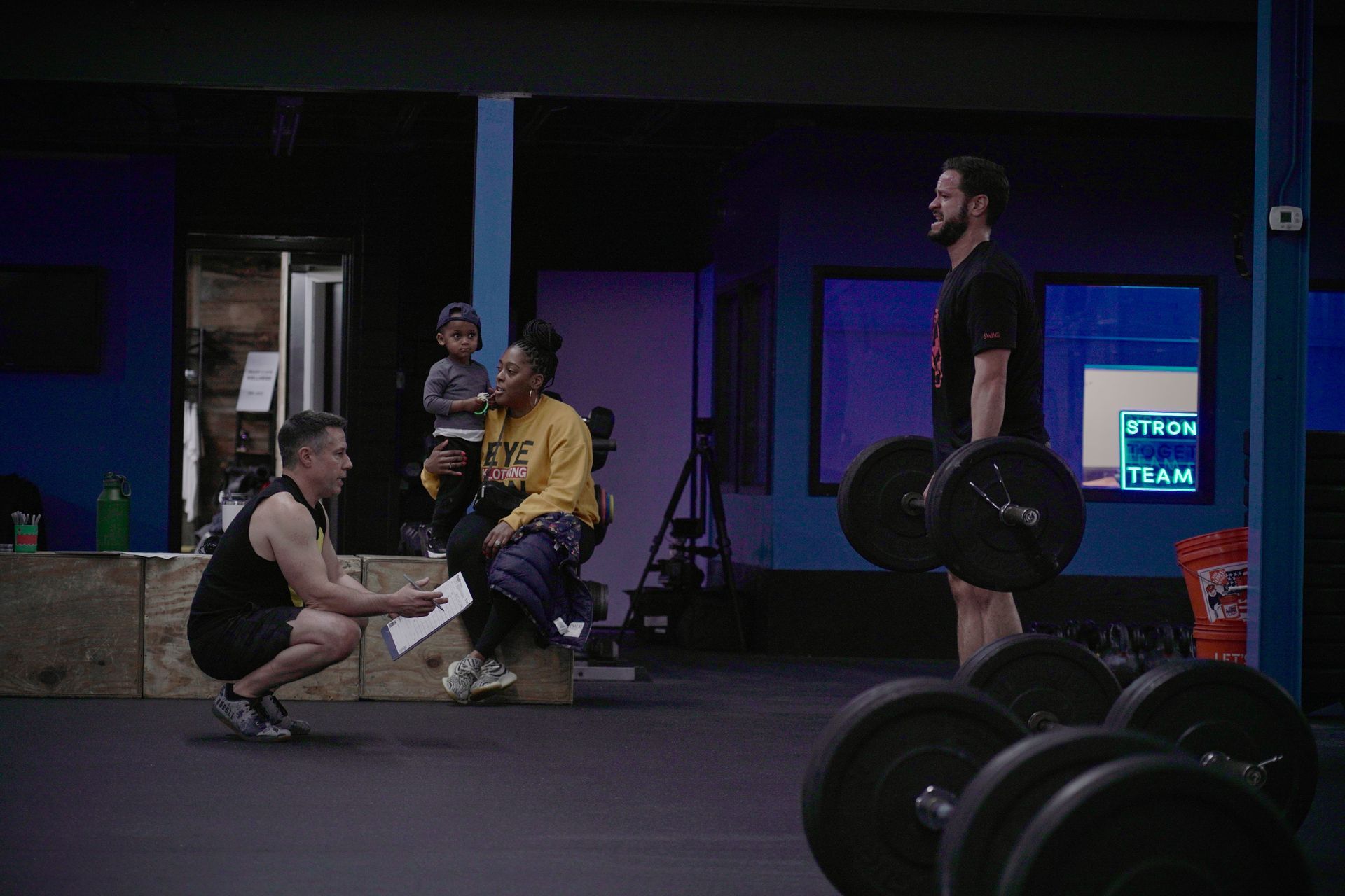 A man is squatting down in front of a group of people in a gym.