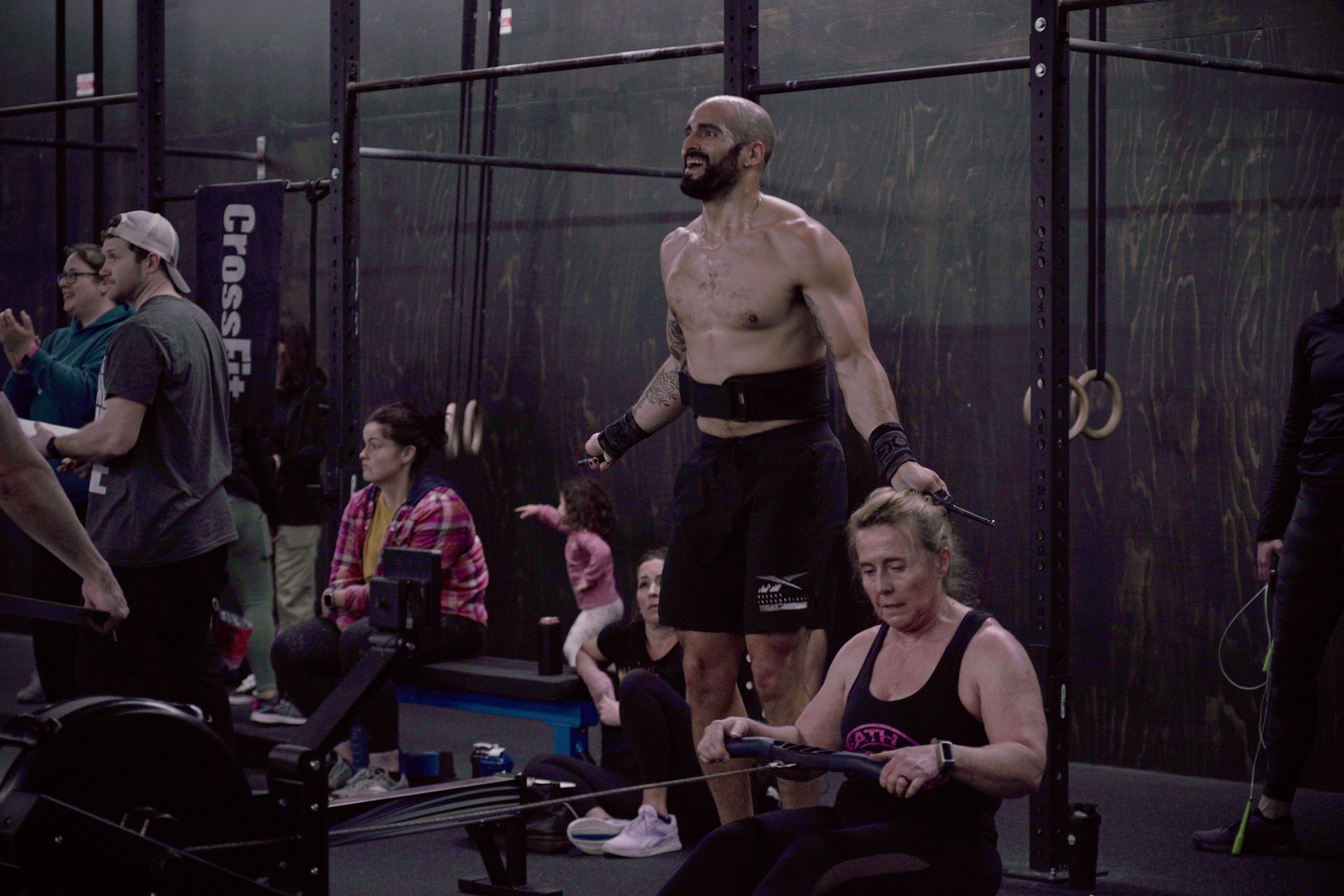 A man without a shirt is standing in front of a group of people in a gym.