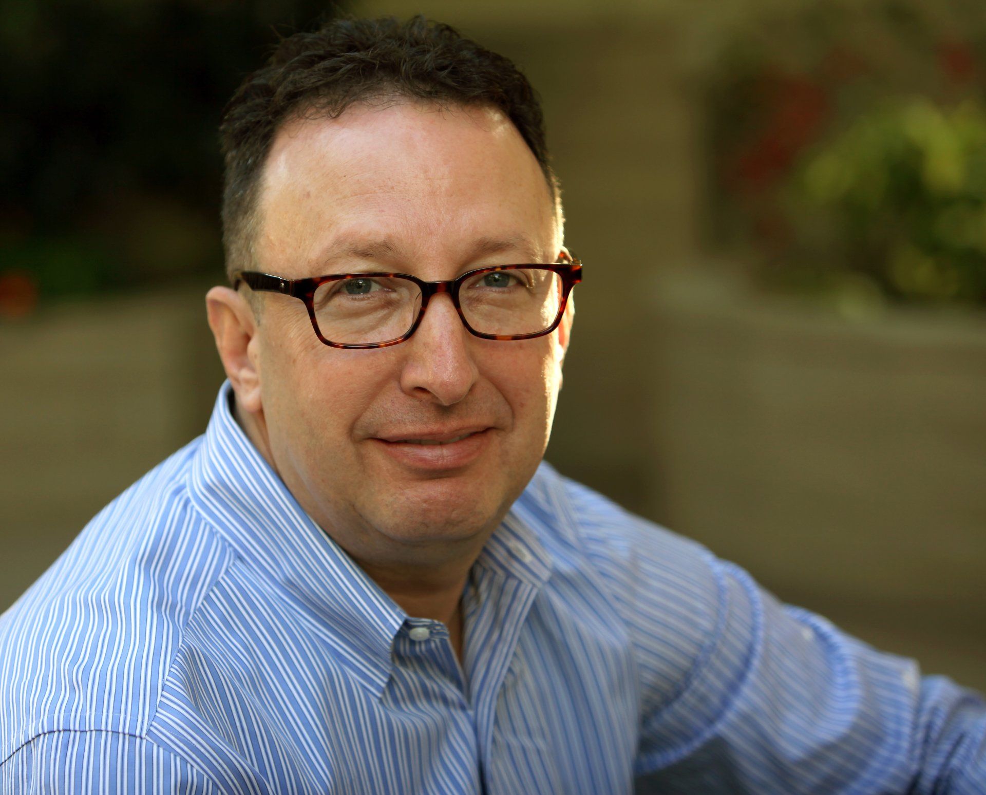 A man wearing glasses and a striped shirt is smiling for the camera - Marc Korody's Picture