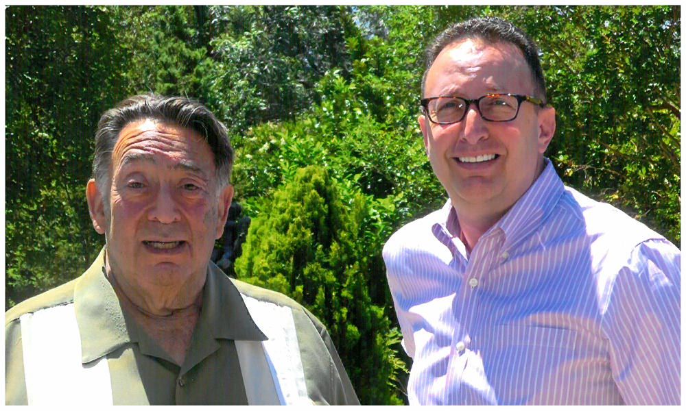 Two men are posing for a picture in front of trees.