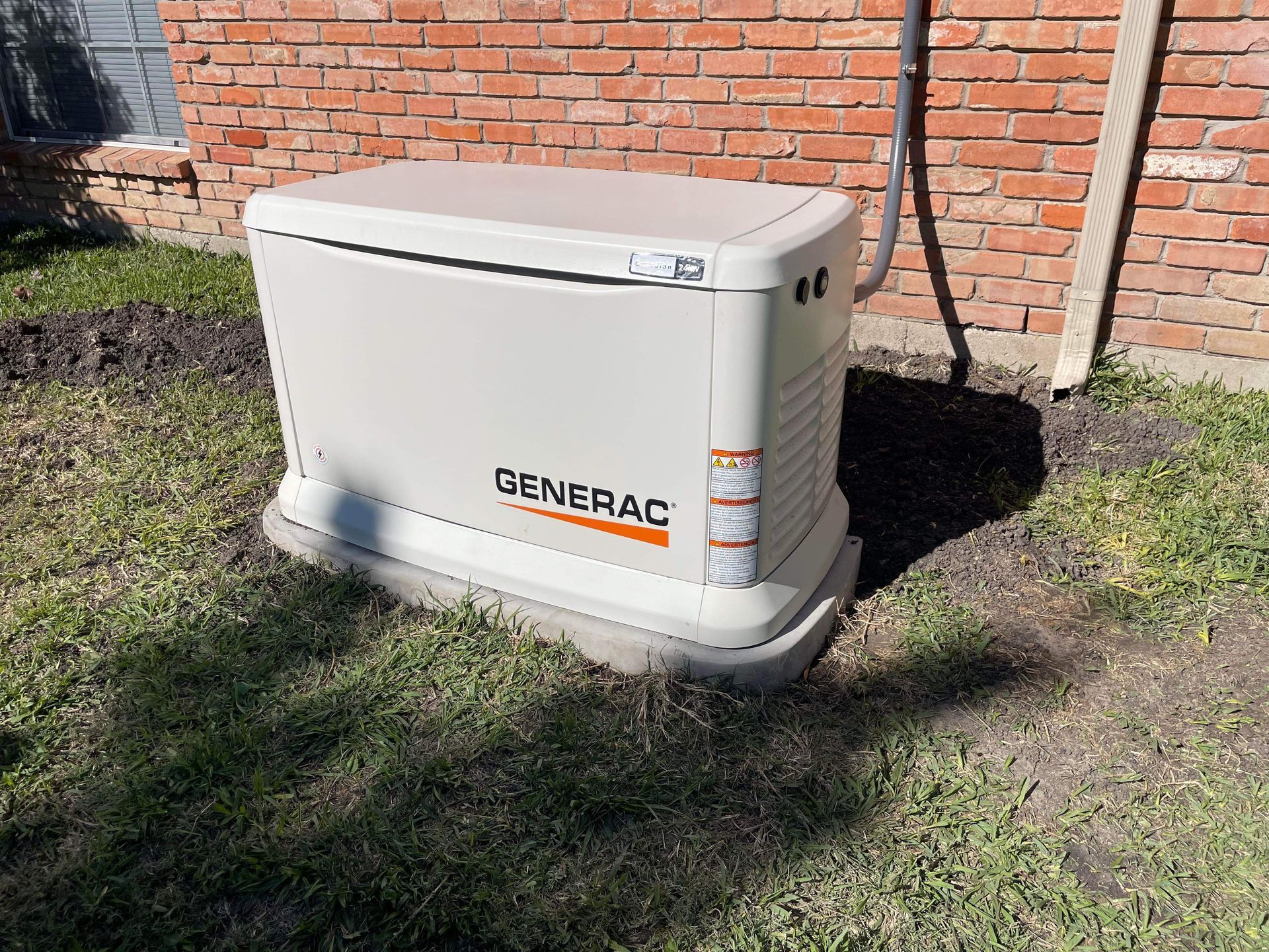 A generator is sitting in the grass in front of a brick building.