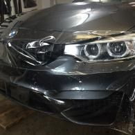 Front of a black car with a damaged hood and headlight, wrapped in protective plastic.