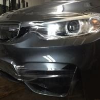 Close-up of a black car’s front bumper and headlight in a dim garage.