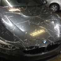 Cracked windshield and shattered front hood of a black BMW in a parking garage
