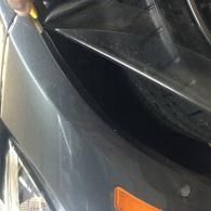 Close-up of a black car’s front corner with a headlight and orange side marker.