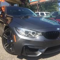 Dark gray BMW sedan parked outdoors, front-left view, with black wheels and headlights on.