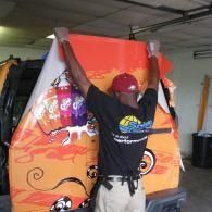 Man in red hard hat standing on a ladder, stretching a large colorful banner in a garage.