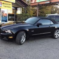 Black Ford Mustang convertible parked outside a window tinting shop
