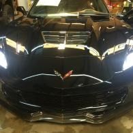 Front view of a black Chevrolet Corvette with headlights on in a garage