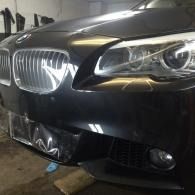 Front view of a black BMW with a damaged front bumper in a garage