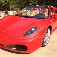 Red Ferrari convertible parked outdoors in sunlight, with tan interior and potted plants in the background