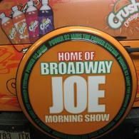Orange van sign reading “Home of Broadway Joe Morning Show” in bold white and green text