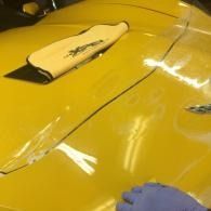 Yellow car body panel with a white hood scoop and reflected light streaks