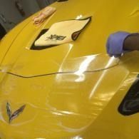 Yellow sports car hood being polished by a gloved hand