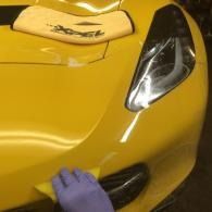 Gloved hand cleaning the front bumper of a yellow sports car
