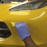 Gloved hand smoothing a yellow car bumper with clear protective film applied