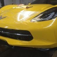 Close-up of a yellow sports car’s front end with black grille and headlights indoors