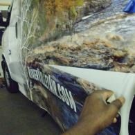 Hand holding the side panel of a muddy white vehicle with a blue banner.