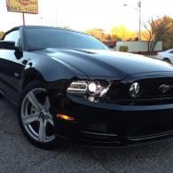 Black sports car parked outdoors at dusk, front view with headlights on