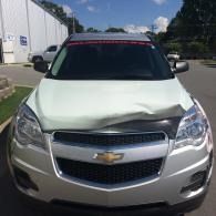 Front view of a white Chevrolet sedan with a dented hood parked outdoors.