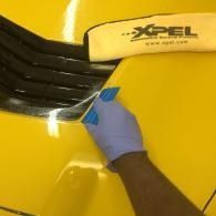Gloved hand applying tape to a yellow XPEL car panel near black trim