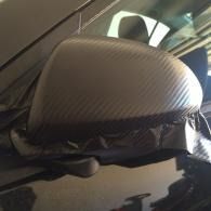 Close-up of a car side mirror wrapped in clear plastic, with a patterned gray cover.