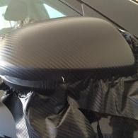 Close-up of a carbon fiber car side mirror wrapped in black plastic.