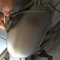 Hand holding a black carbon-fiber textured hard-shell case in a car interior