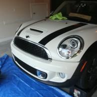 White Mini Cooper with black racing stripes parked in a garage, front view