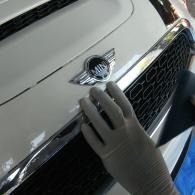 Gloved hand cleaning the chrome grille and hood emblem of a white Mini car