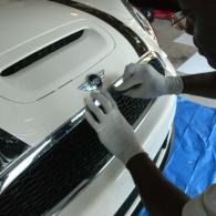 Hands fitting a chrome emblem on the front grille of a white car