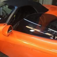 Orange sports car with black soft top and rear window, viewed close-up indoors