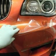 Gloved hand pressing dented orange car bumper near the headlight