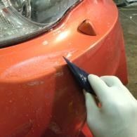 Hand scraping orange car bumper paint with a utility knife