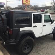 White Jeep Wrangler with black hardtop parked outdoors near a roadside sign.