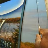 Hand peeling a clear protective film from a reflective window with landscape graphics