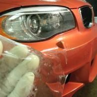 Close-up of an orange car bumper being wrapped or repaired with clear plastic film