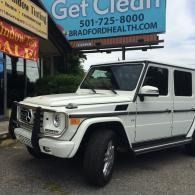 White Mercedes G-Class SUV parked outside near a sign.