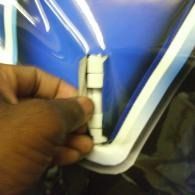 Hand holding a small white hinge on a blue and white plastic panel